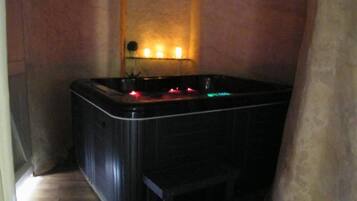 Een kamer met een badkuip, een houten plank met kaarsen en een kleine tafel.