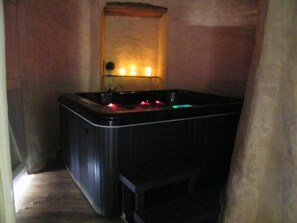 Une pièce avec une baignoire, une étagère en bois ornée de bougies et une petite table.