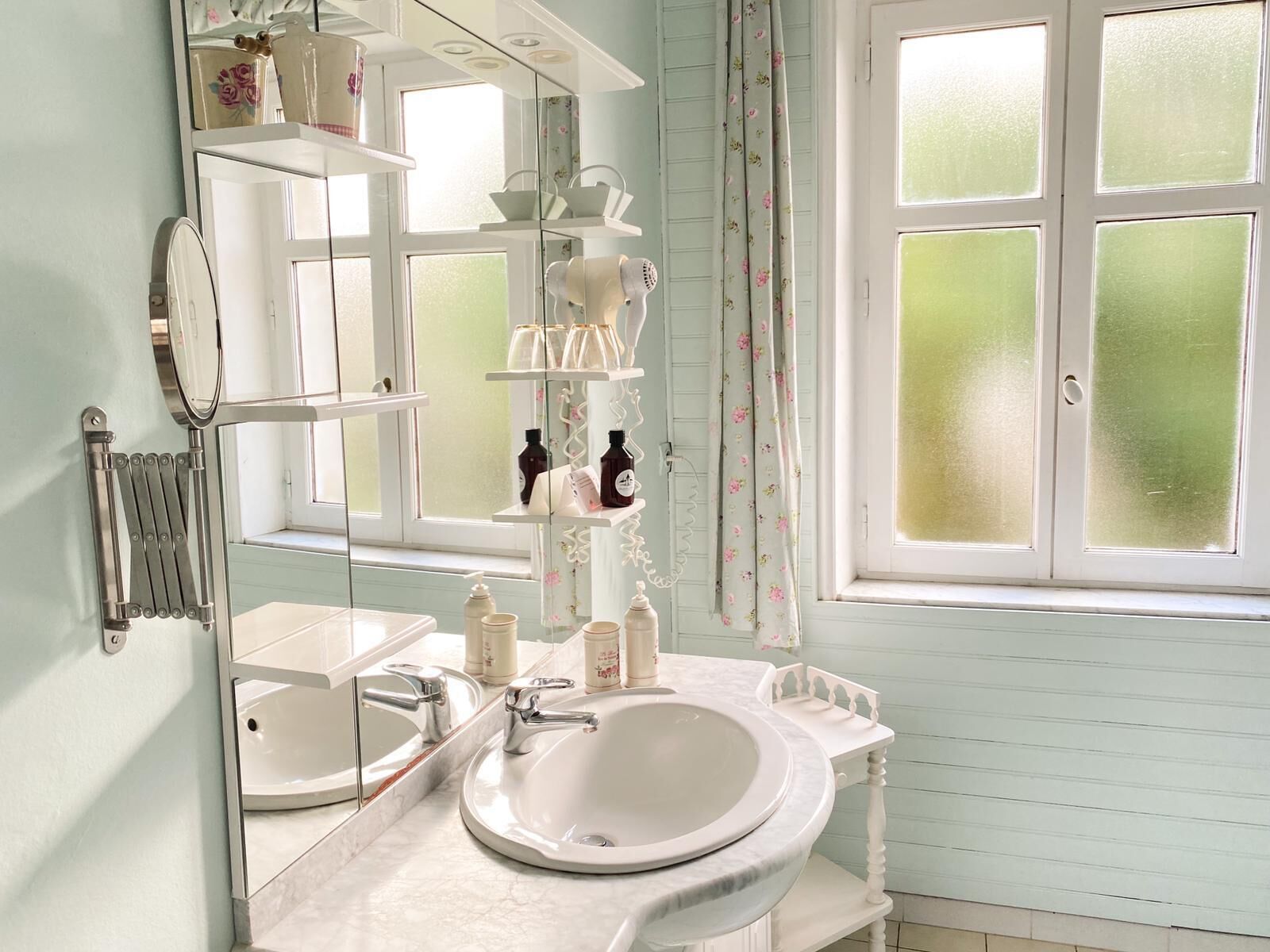 A bathroom with a large mirror, two sinks, and shelves with toiletries.