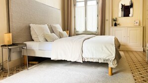 Een netjes ingerichte slaapkamer met een bed, nachtkastje, lamp en uitzicht op de badkamer.