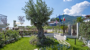 A landscaped garden with a large tree, a stone pathway, and a metal fence. - Villa Paradise Resort (Agerola)
