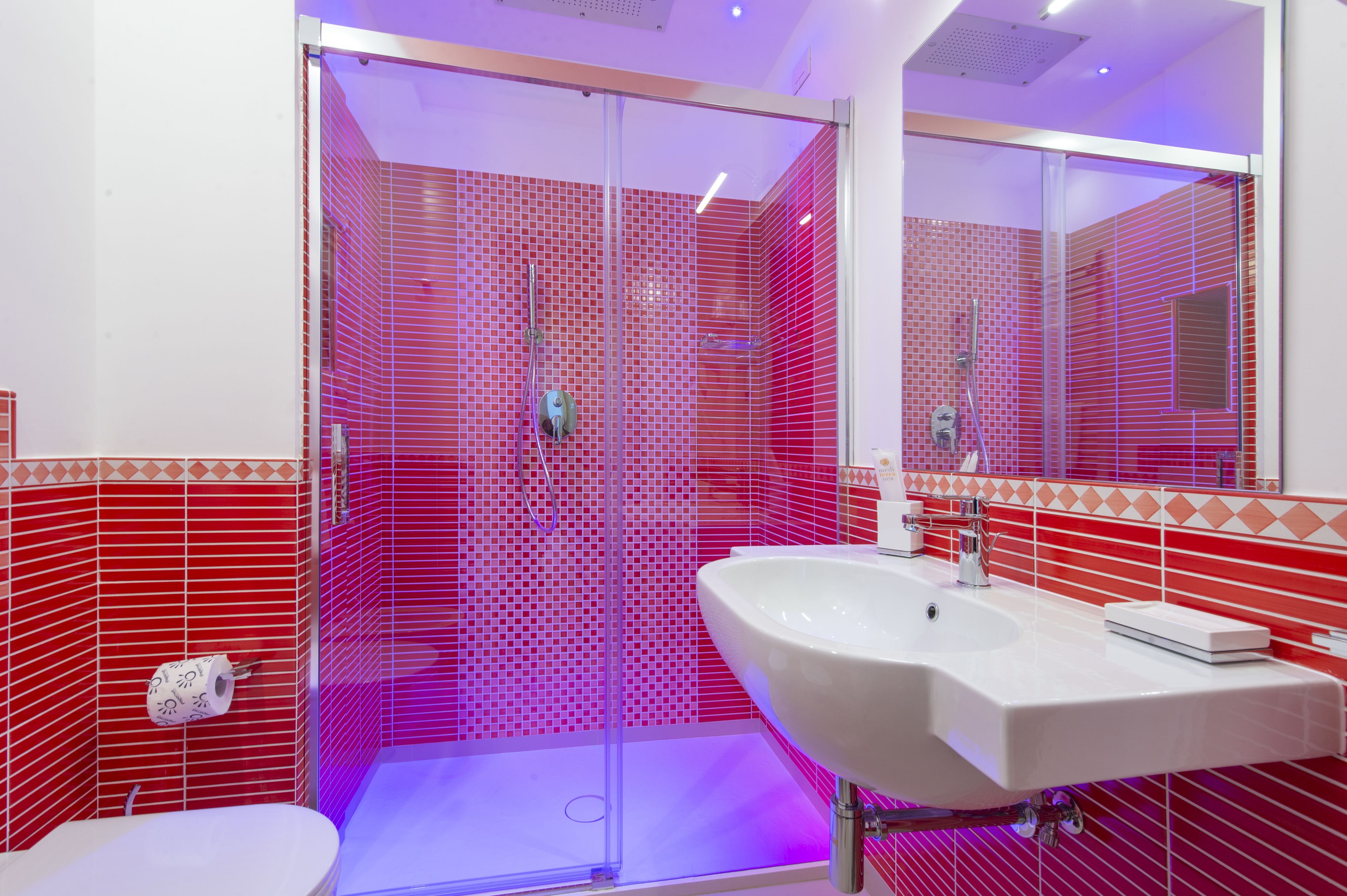 Une salle de bain moderne avec une douche en verre, un lavabo blanc et des murs recouverts de carreaux rouges.