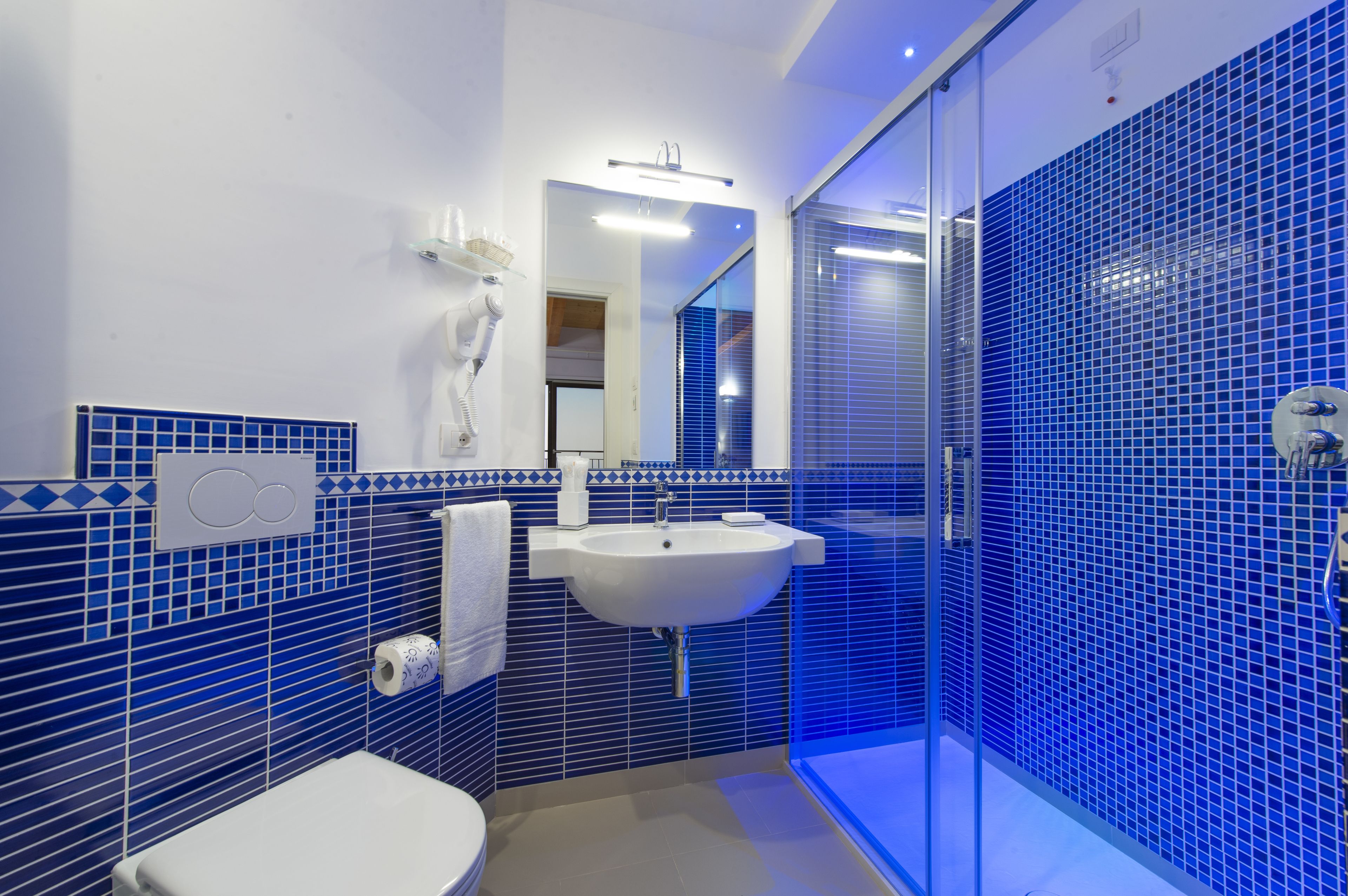 Une salle de bain moderne avec un lavabo blanc, des murs recouverts de carreaux bleus et une douche en verre.
