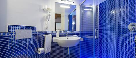 Une salle de bain moderne avec un lavabo blanc, des murs recouverts de carreaux bleus et une douche en verre.