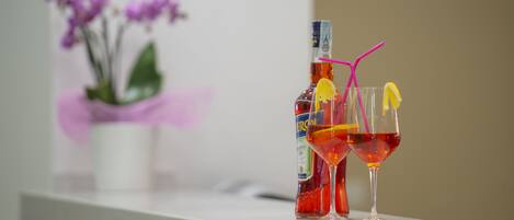 A bottle of red wine and two glasses on a white surface with a potted plant in the background.