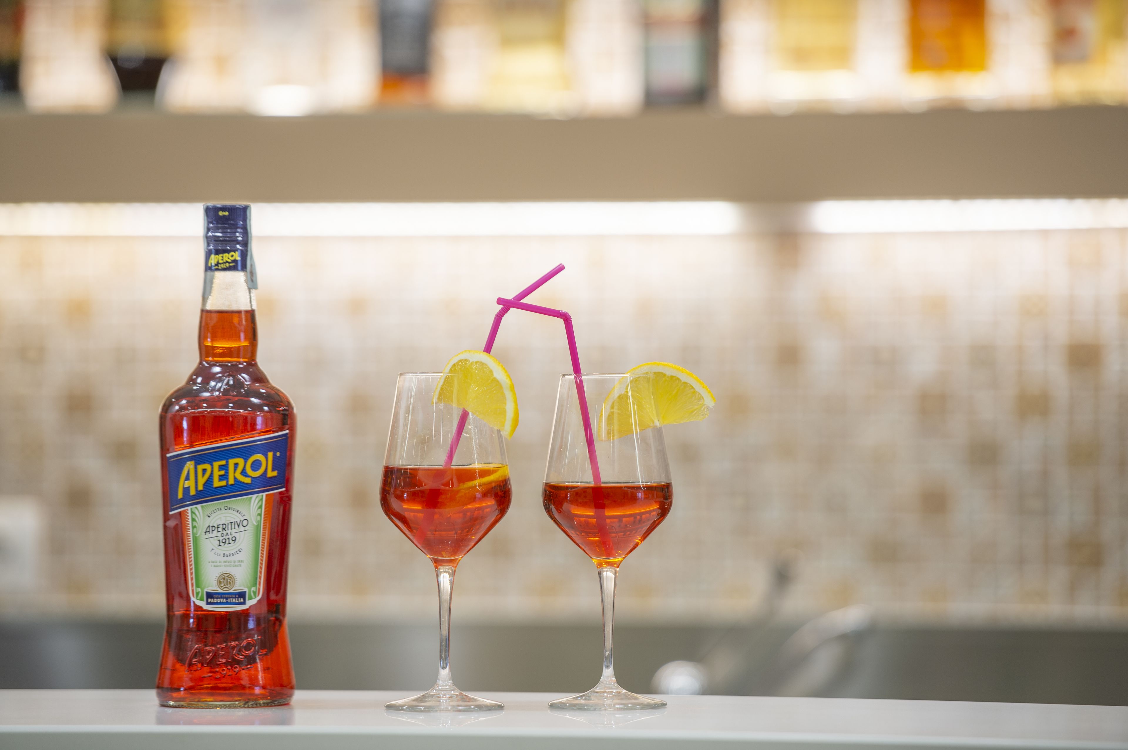 A bottle of Aperol and two glasses with straws and lemon slices.