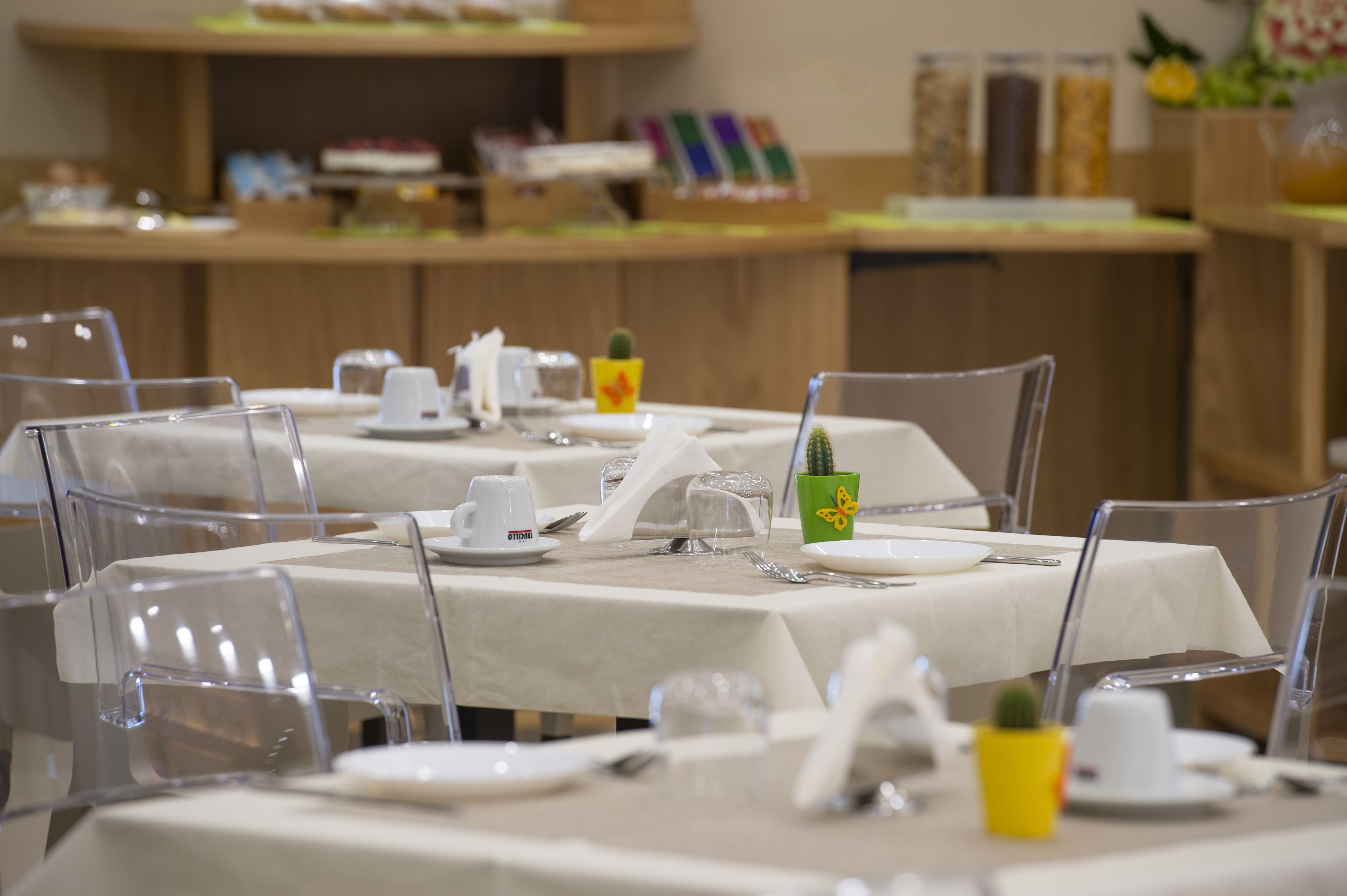 Un restaurant avec des tables dressées pour le service, des chaises transparentes et un comptoir où sont exposés divers articles.