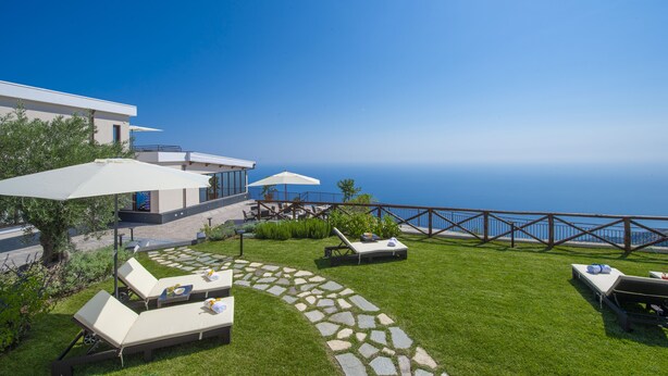 A modern outdoor patio with lounge chairs, umbrellas, and a stone pathway. - Villa Paradise Resort (Agerola)