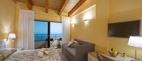 A hotel room with a bed, a sofa, a desk, and a TV. There is a balcony with a view.
