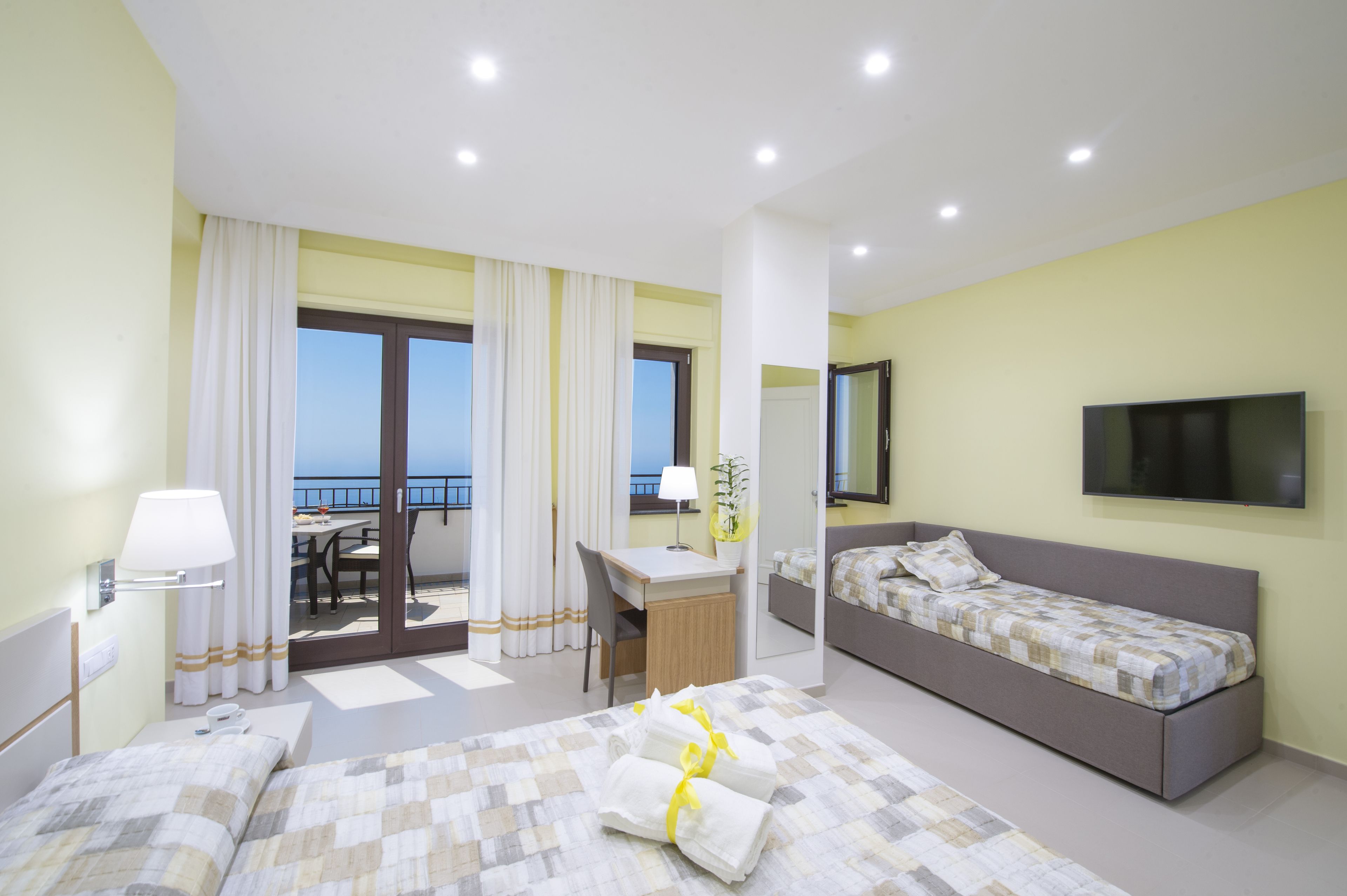 A hotel room with two beds, a desk, a chair, a TV, and a balcony with curtains.