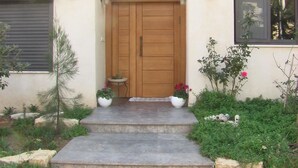 Una casa con puerta principal de madera, una pequeña mesa con planta en maceta y una ventana con vista al cielo.
