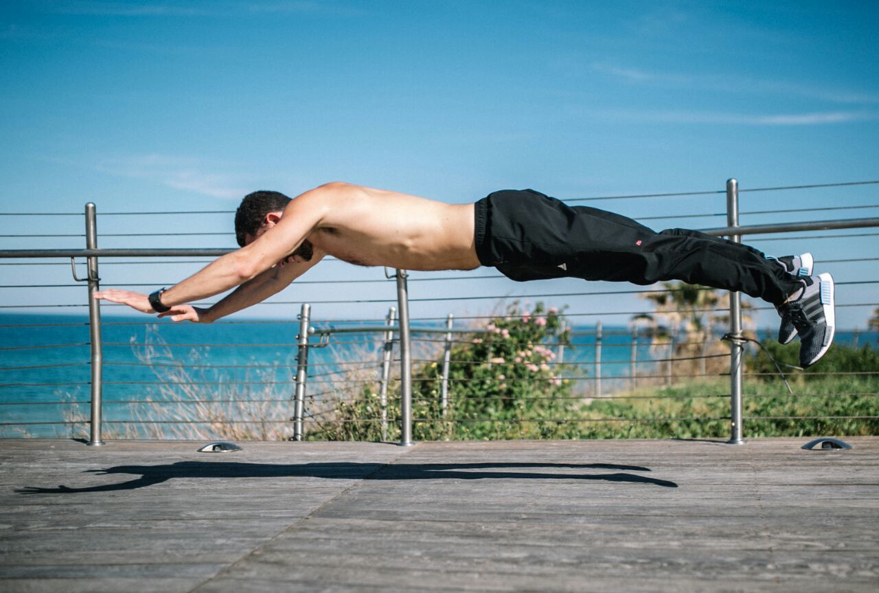 Een man doet een push-up aan een metalen stang, met uitzicht op de kust op de achtergrond.