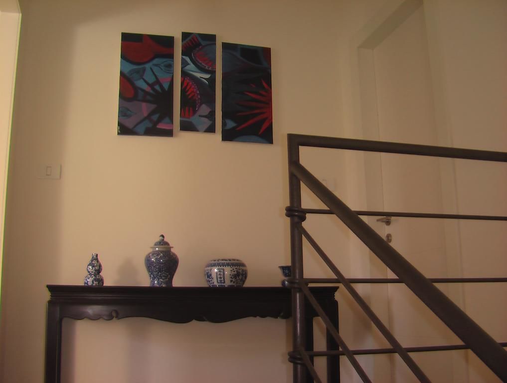 A staircase with a dark metal railing, a wall-mounted shelf with decorative items, and three abstract paintings above the shelf.