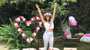 Una persona de pie frente a un letrero que dice 'BRIDE' hecho de rosas, con un arreglo de rosas en forma de corazón sobre el letrero.