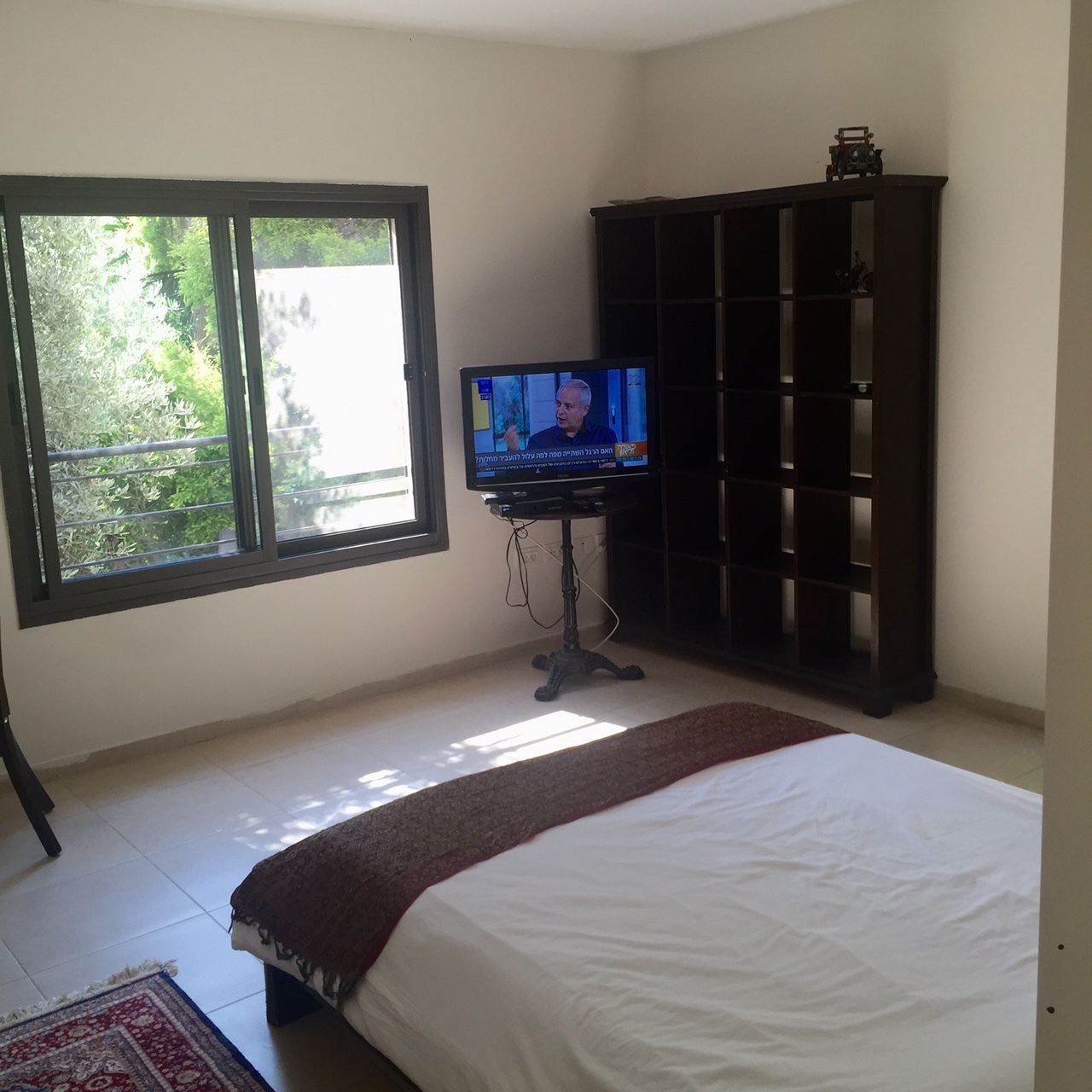 Un dormitorio con una cama, un televisor sobre un mueble, una ventana y un armario de madera oscura.
