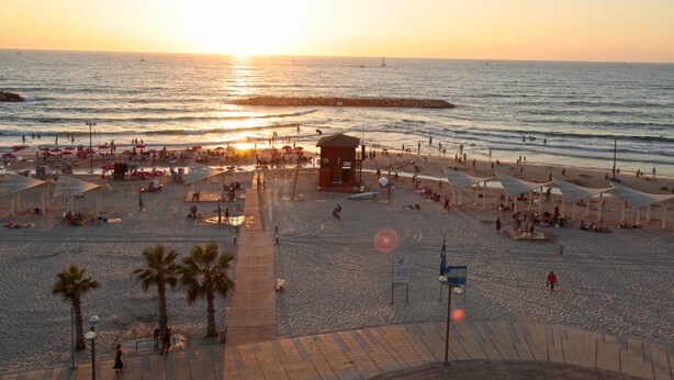 Una playa con sombrillas, una torre de salvavidas y gente disfrutando del atardecer.