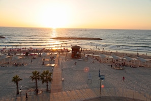 Una playa con sombrillas, una torre de salvavidas y gente disfrutando del atardecer.