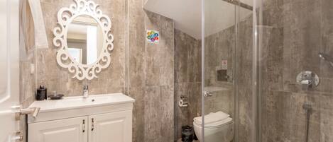 Un baño moderno con tocador blanco, un espejo grande y cabina de ducha con mampara de vidrio.