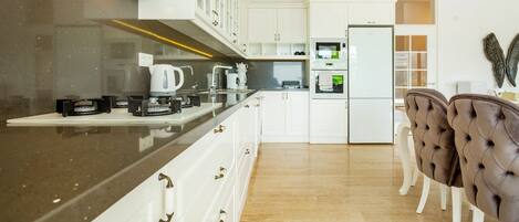 A modern kitchen with white cabinetry, a black countertop, and a dining area with two chairs.