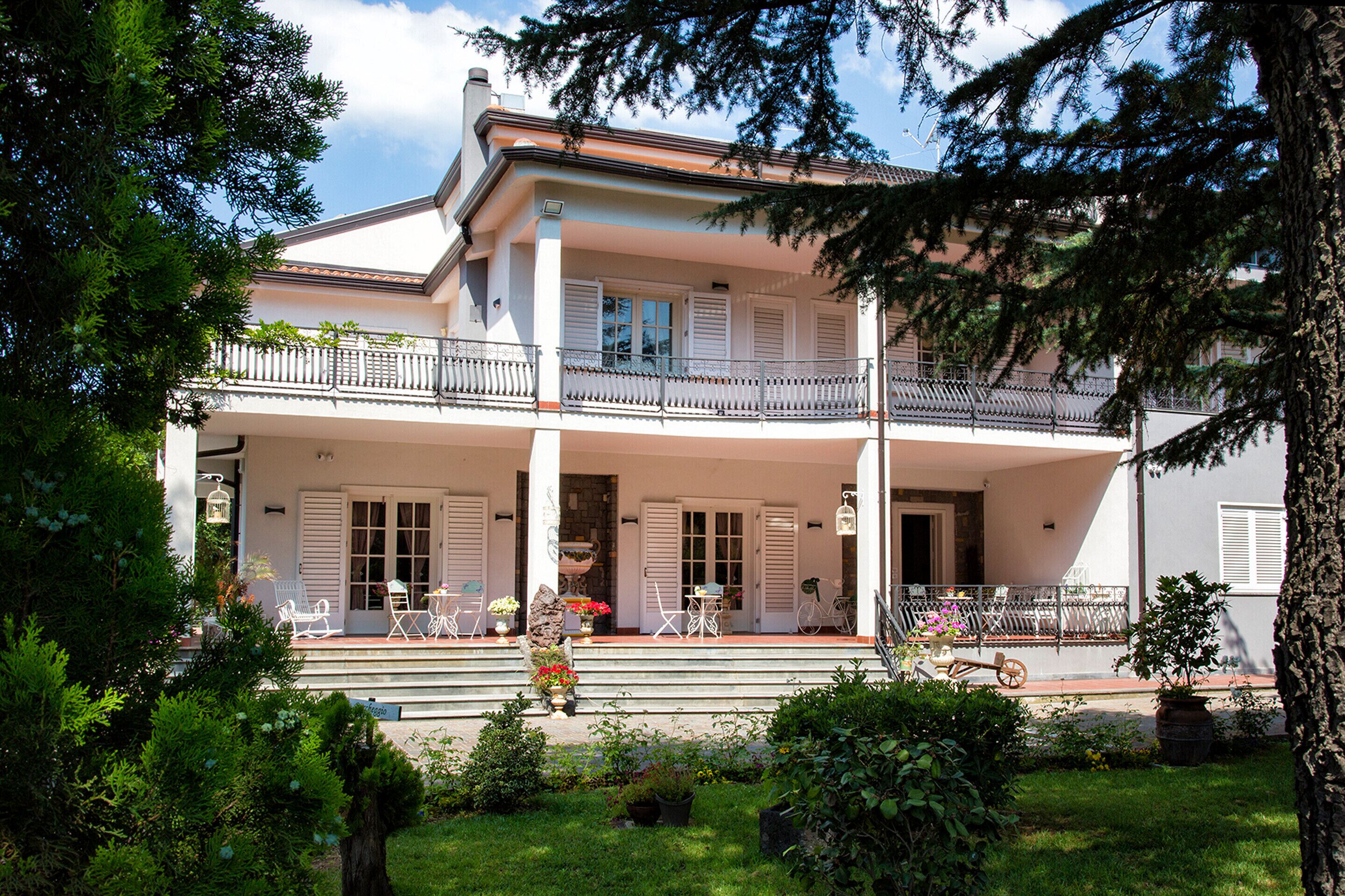 A two-story building with a balcony, a garden in the foreground, and a clear sky.
