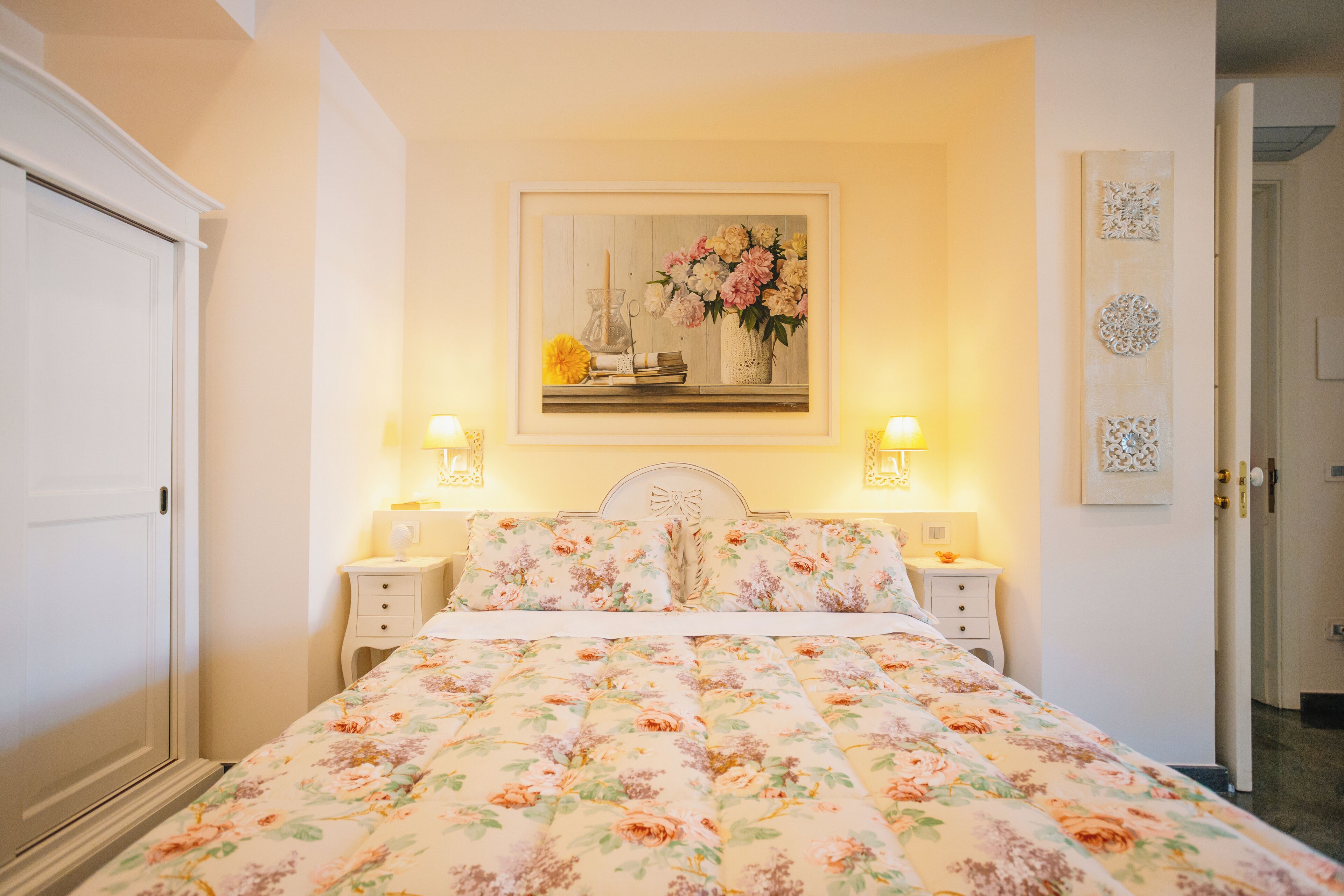 Una camera da letto con copripiumino floreale, un quadro appeso sopra il letto e due abat-jour.