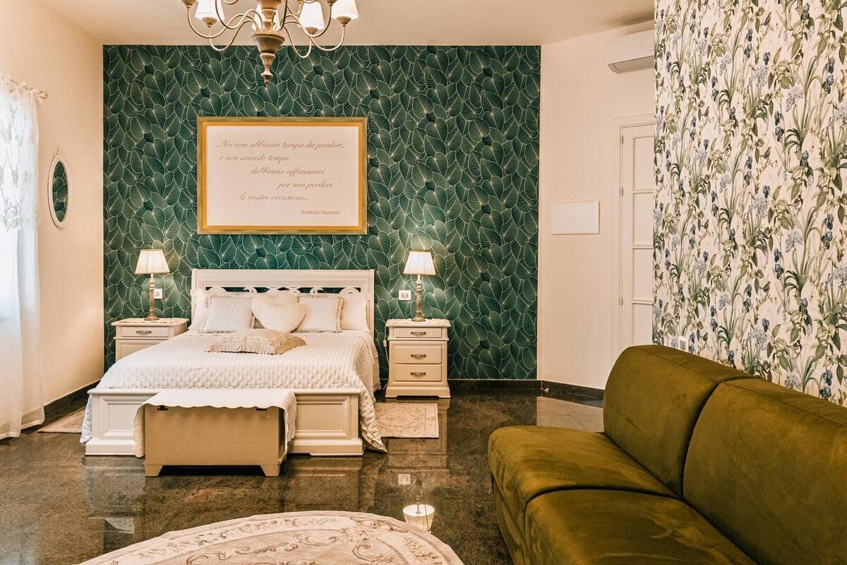 Une chambre à coucher avec un lit, des tables de chevet, un mur vert, un lustre et un canapé vert.