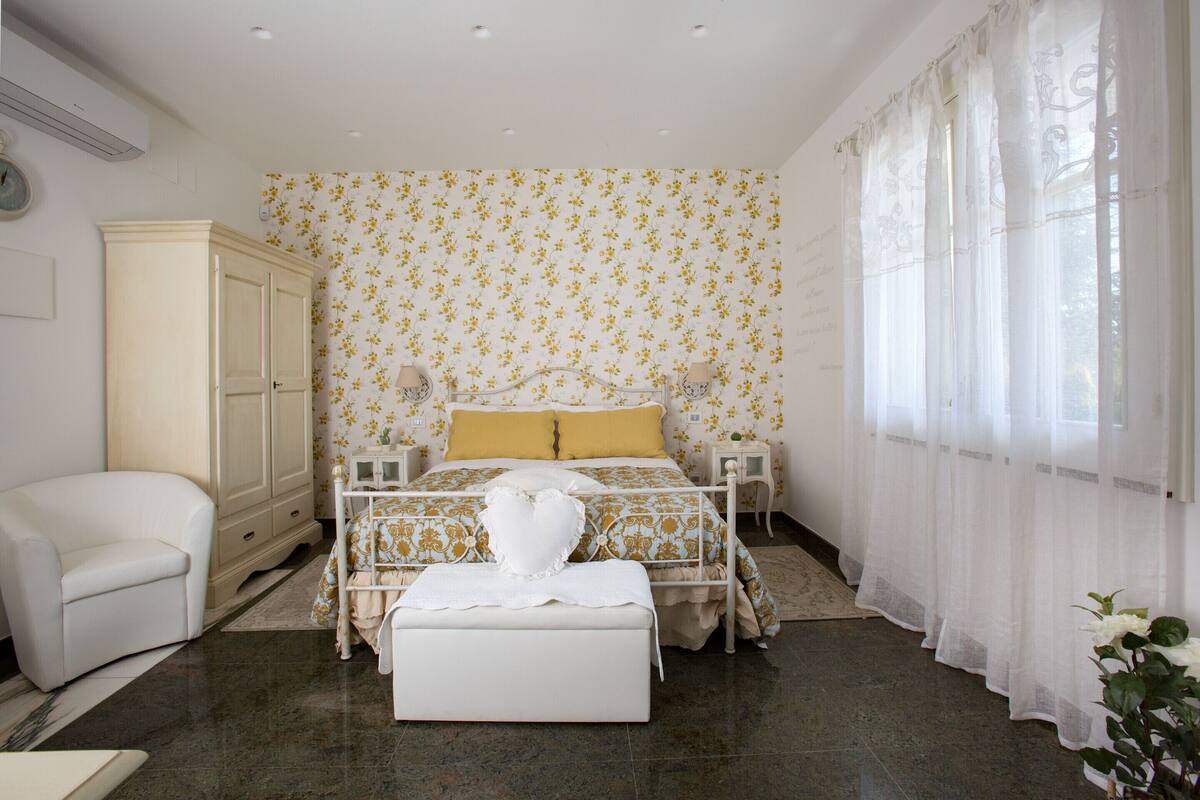 Une chambre à coucher comprenant un lit, une table de chevet, une commode, une armoire, une chaise et une fenêtre avec des rideaux.