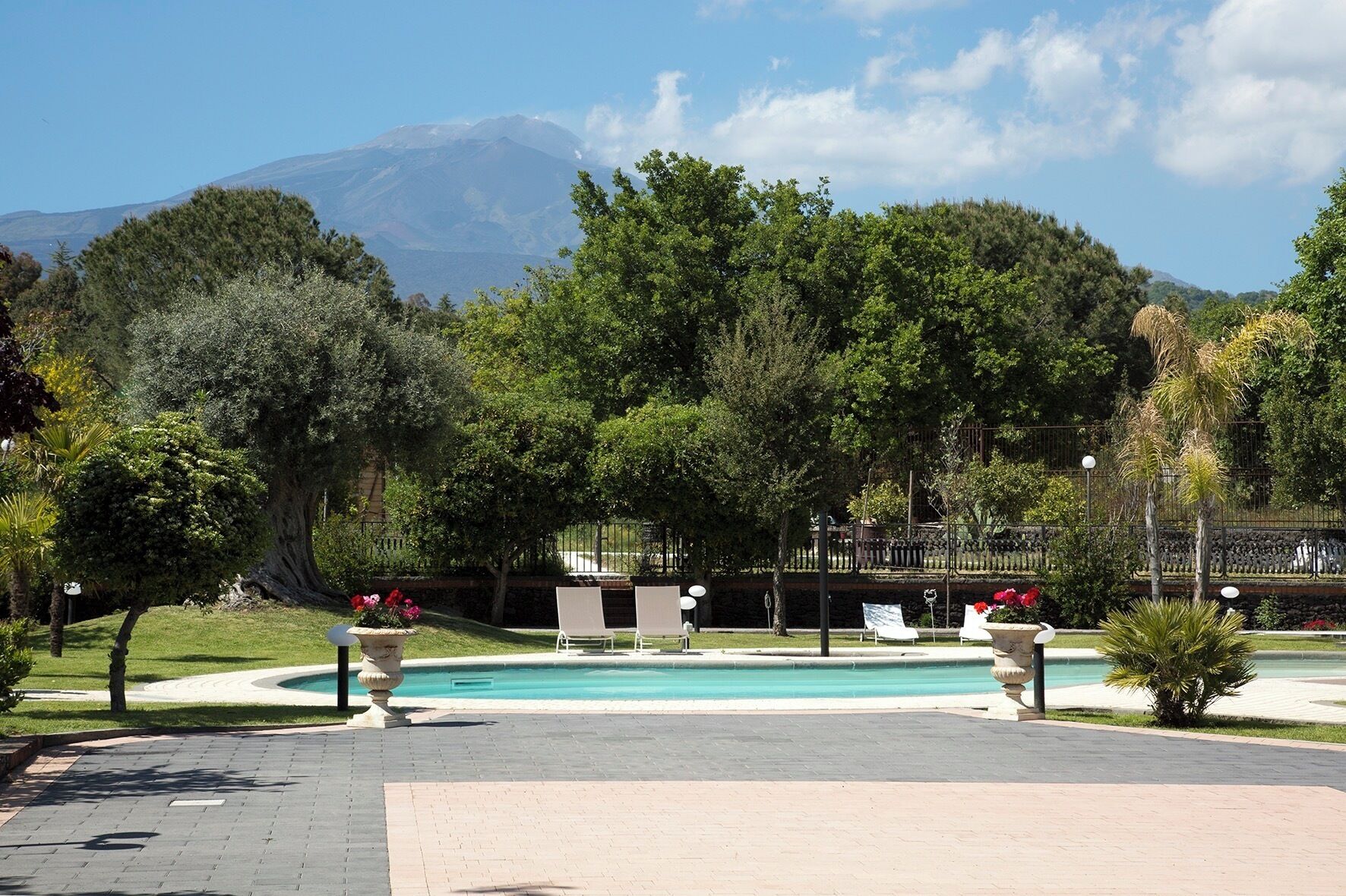 A pool area with a mountain in the background, surrounded by trees and a fence.