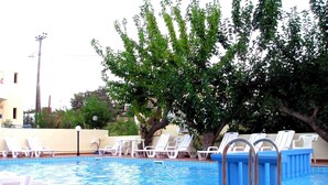 A swimming pool with white lounge chairs and a tree in the background. - Marianthi studios (Chania)