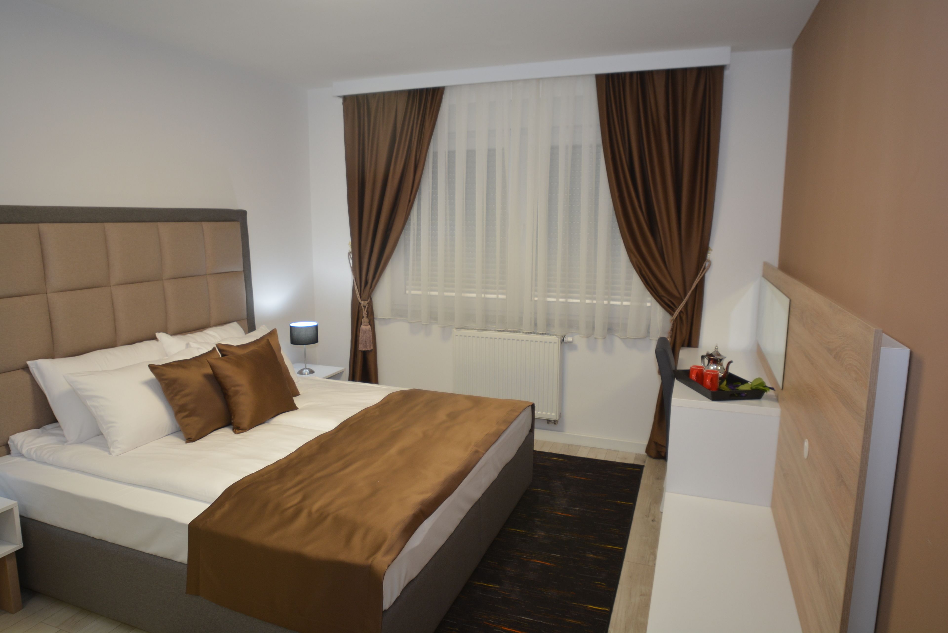 A modern hotel room with a large bed, a bedside table with a lamp, and a small seating area with a table and chairs.
