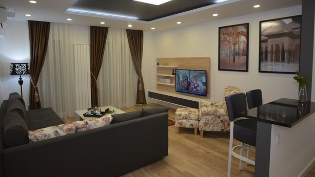 A modern living room with a sofa, a coffee table, a TV, and a dining area with chairs. - Hotel Family (Sarajevo)