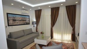 A modern living room with a grey sofa, a glass coffee table, and a red patterned rug. - Hotel Family (Sarajevo)