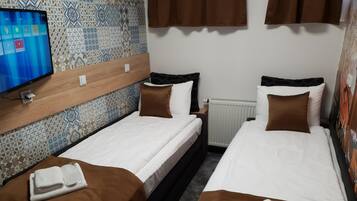 A hotel room with two beds, a television, patterned wall tiles, and a radiator.
