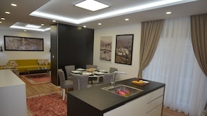 A modern kitchen with a central island, dining area with chairs and a table, and a living area with a sofa and a coffee table. - Hotel Family (Sarajevo)