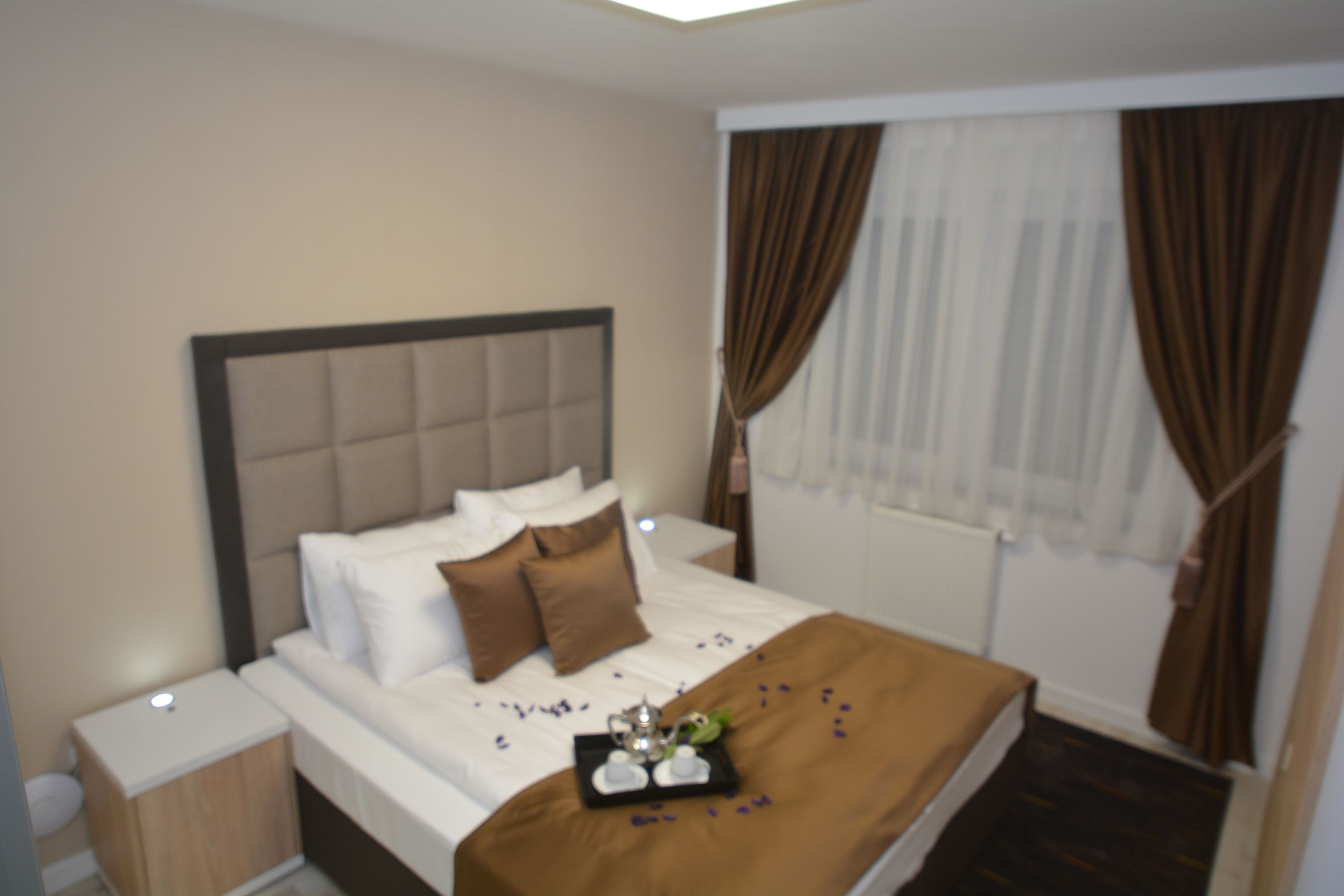 A neatly made bed with a brown headboard, white linens, and a tray with a teapot and cups.