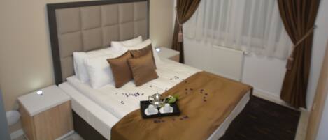 A neatly made bed with a brown headboard, white linens, and a tray with a teapot and cups.