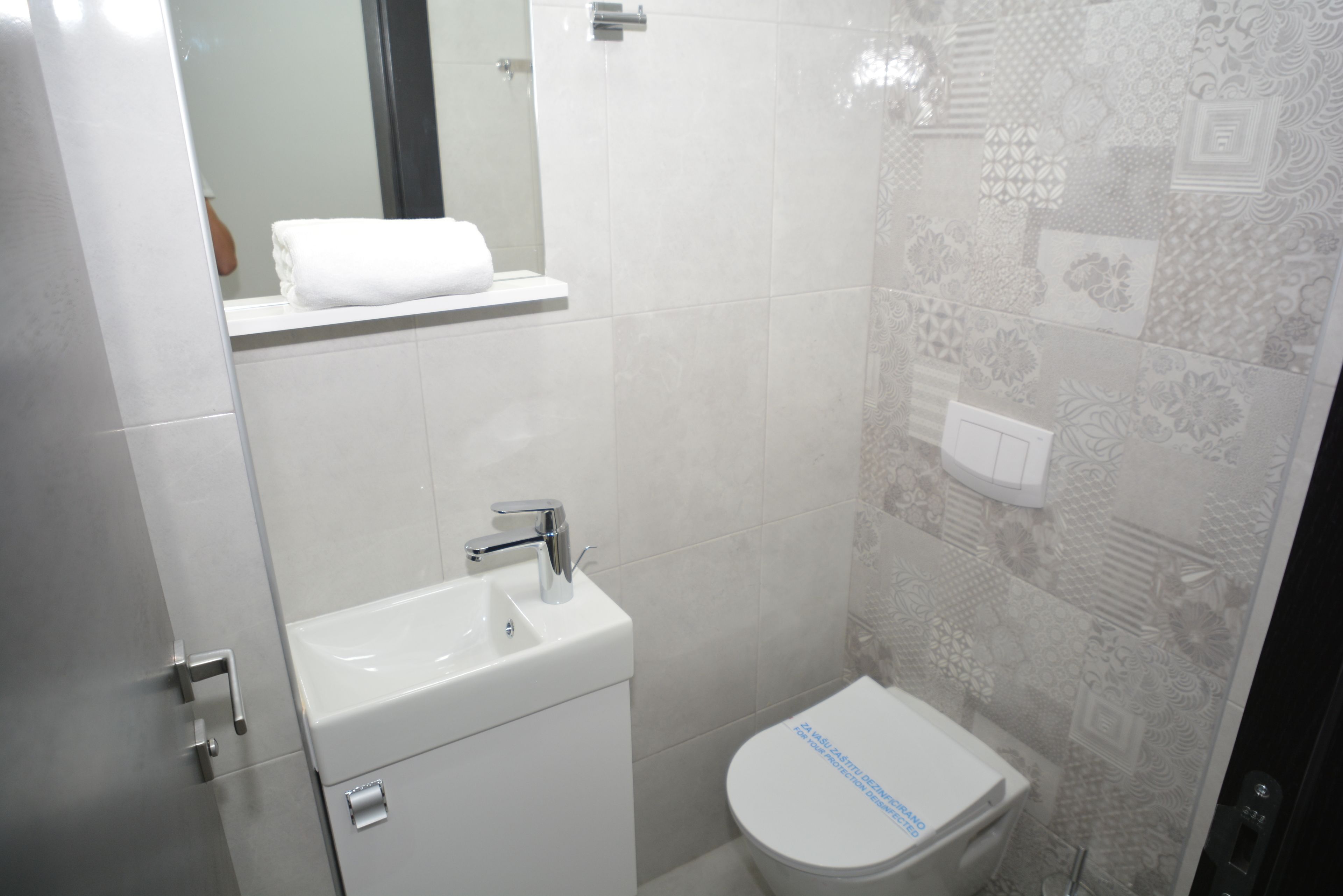 A modern bathroom with a white sink, toilet, and a towel on the shelf.