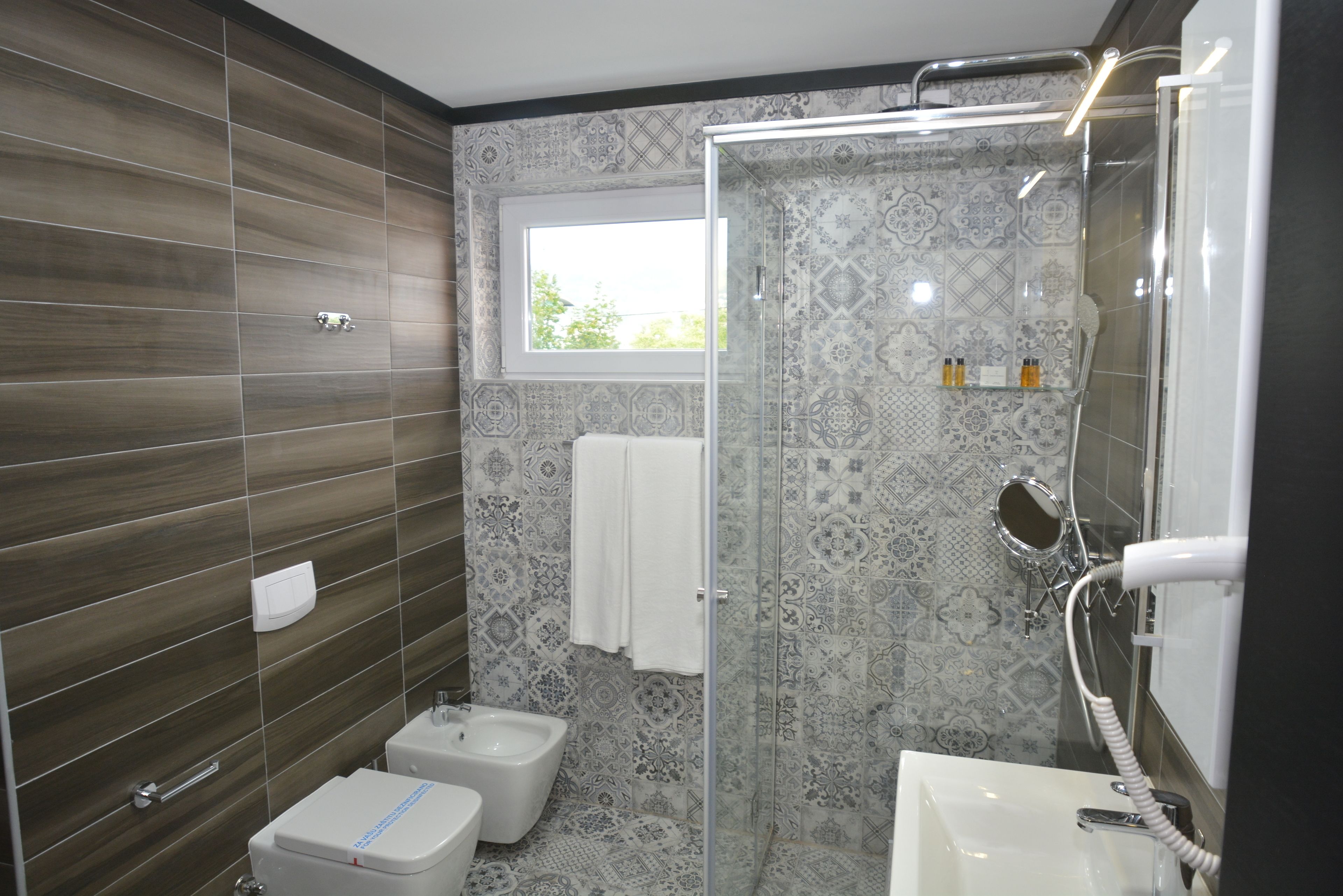 A modern bathroom with a shower, toilet, and sink, featuring patterned tiles and a window.