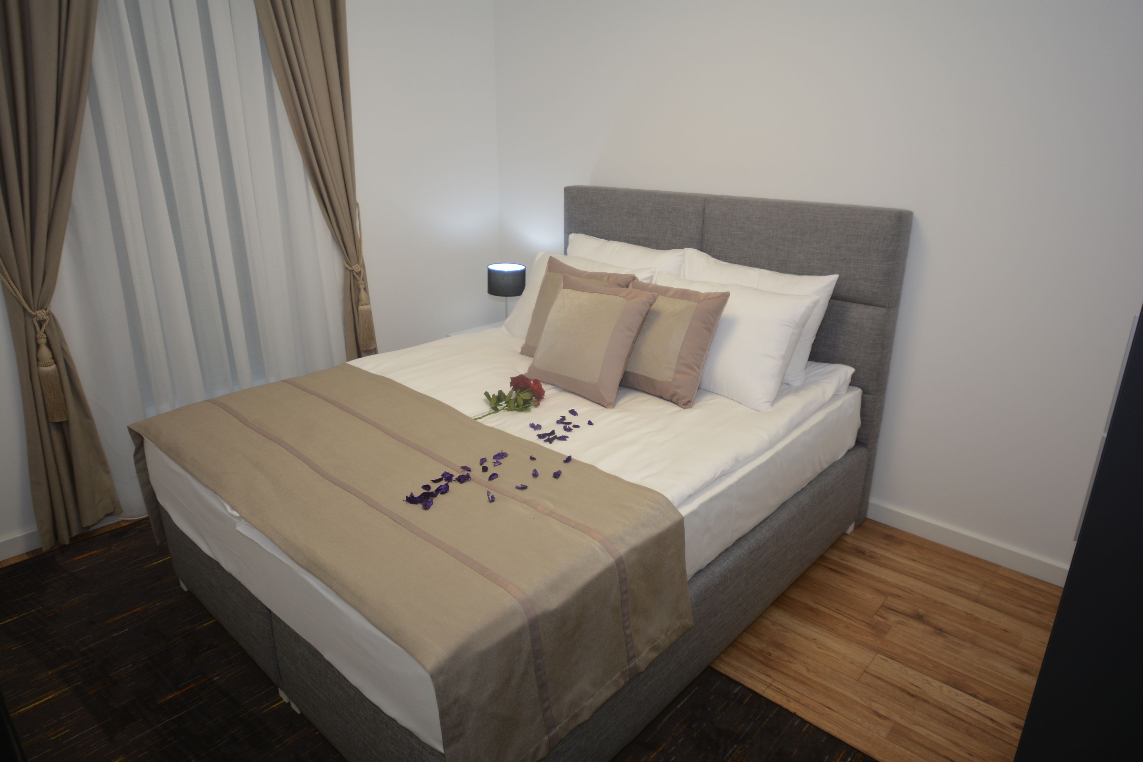 A neatly made bed with a beige bedspread, a grey headboard, and white pillows.