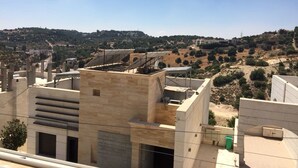 Un bâtiment moderne doté d’un toit plat et de nombreux balcons, entouré d’un paysage vallonné à la végétation clairsemée.