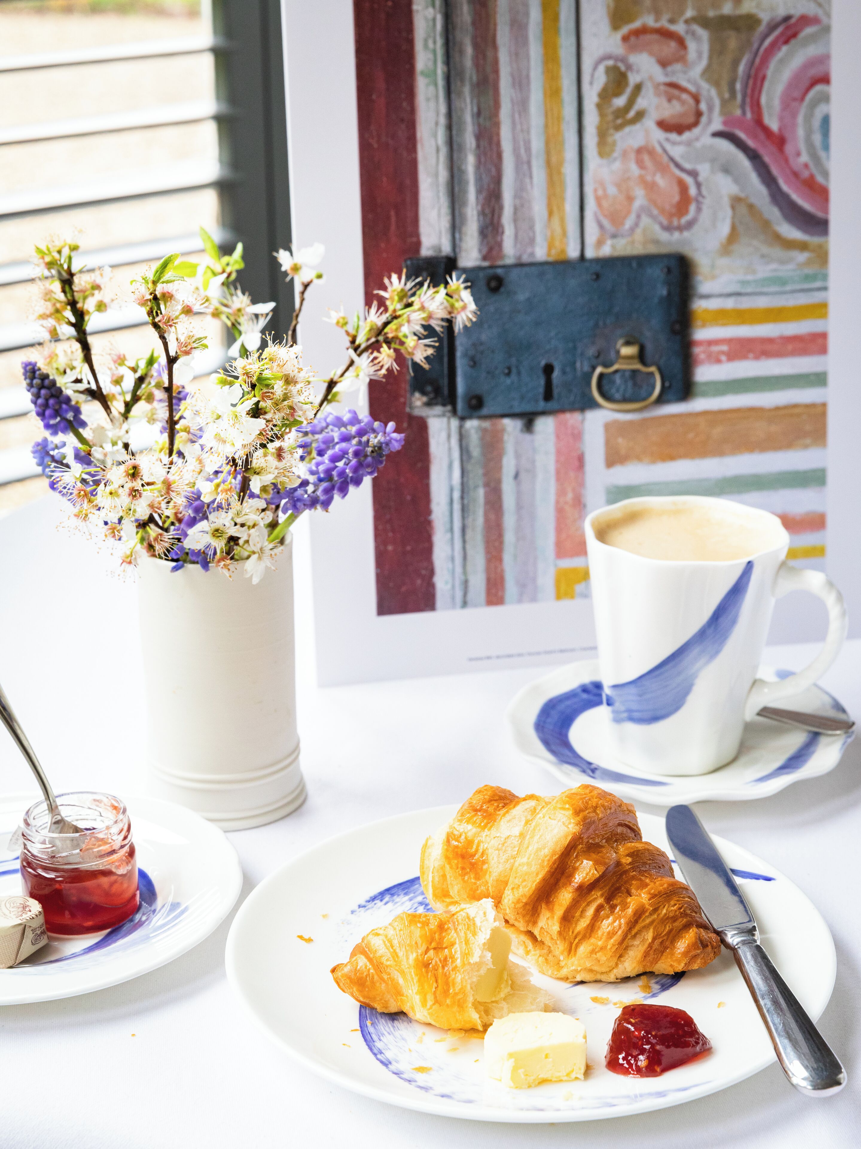 A breakfast setting with croissants, butter, jam, and a cup of coffee on a table.