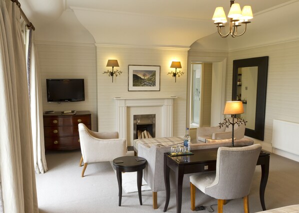 A hotel room with a fireplace, a dining table with chairs, a television, and two wall-mounted lamps. - Tickton Grange Hotel (Beverley)