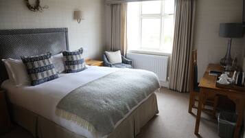 A neatly arranged bedroom with a large bed, a chair, a table, and a window with curtains.