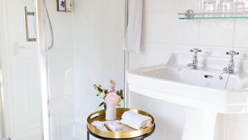 A modern bathroom with a glass shower enclosure, a pedestal sink, and a small round table with toiletries.