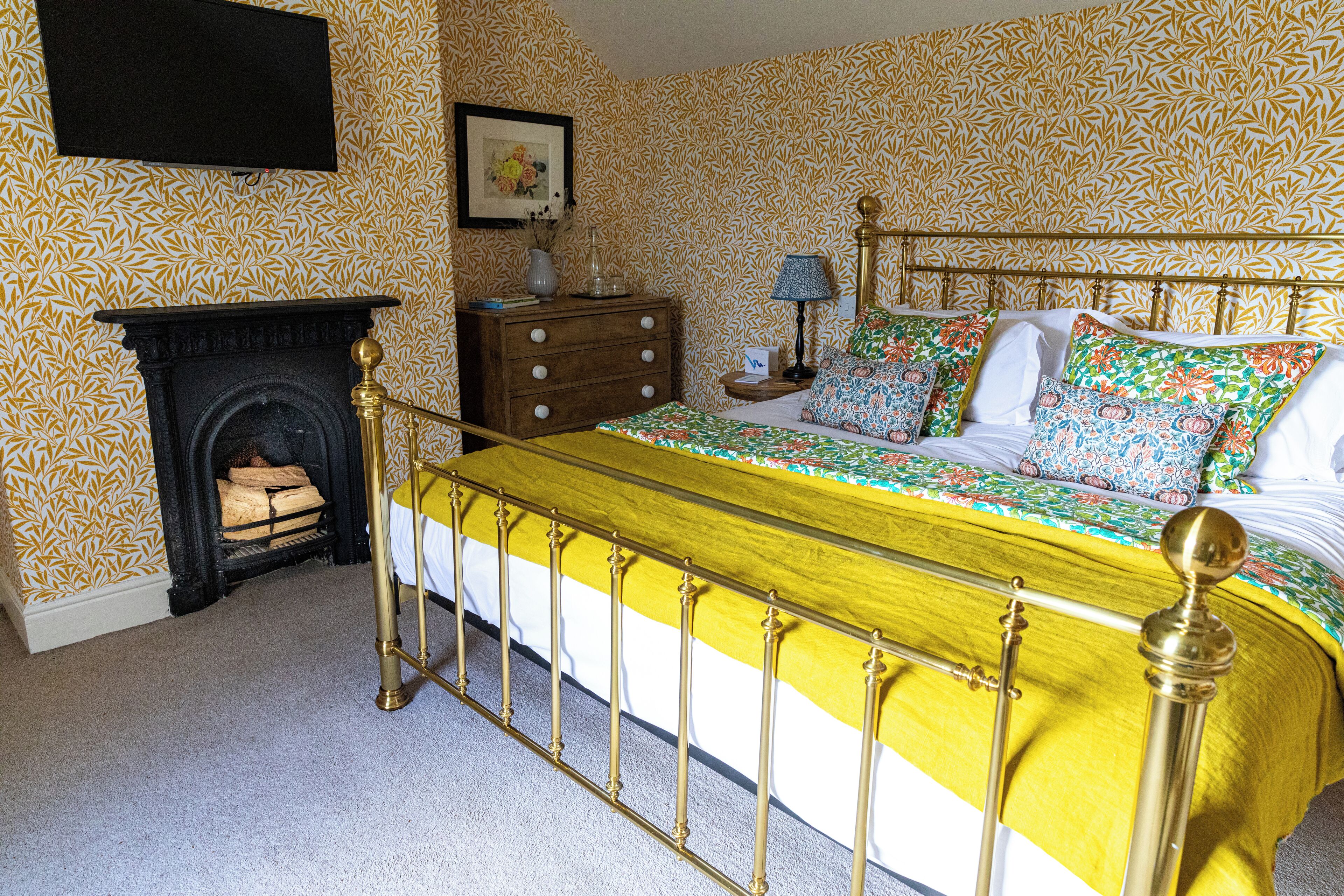 Um quarto com cama, mesa de cabeceira, cômoda, abajur e lareira.