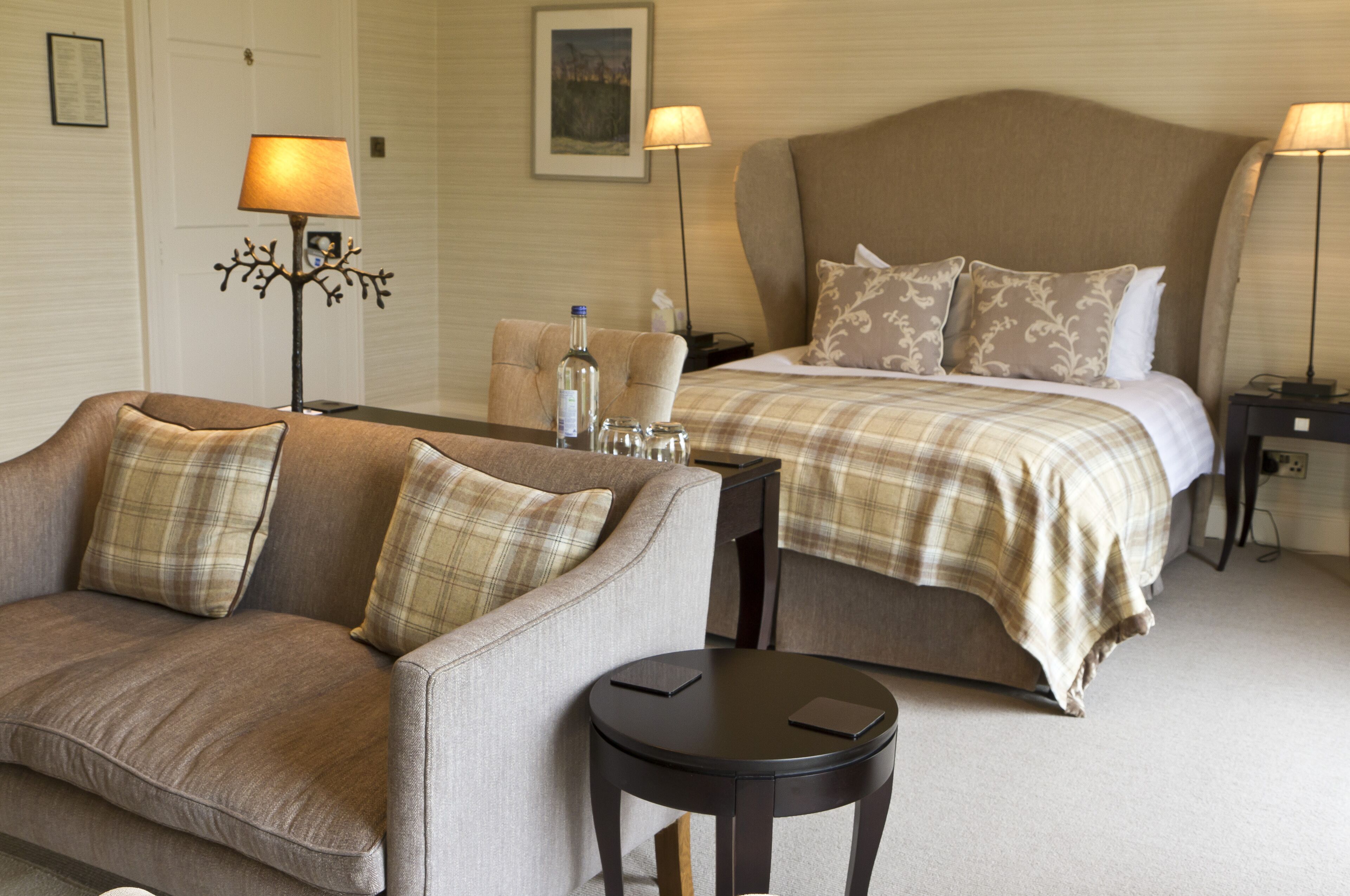 A hotel room with a bed, a sofa, a small table, and two lamps.