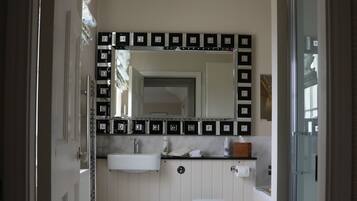 A bathroom with a white toilet, a sink, and a mirror. There is a shower area with a glass door. The floor is tiled, and there are cabinets with black handles.