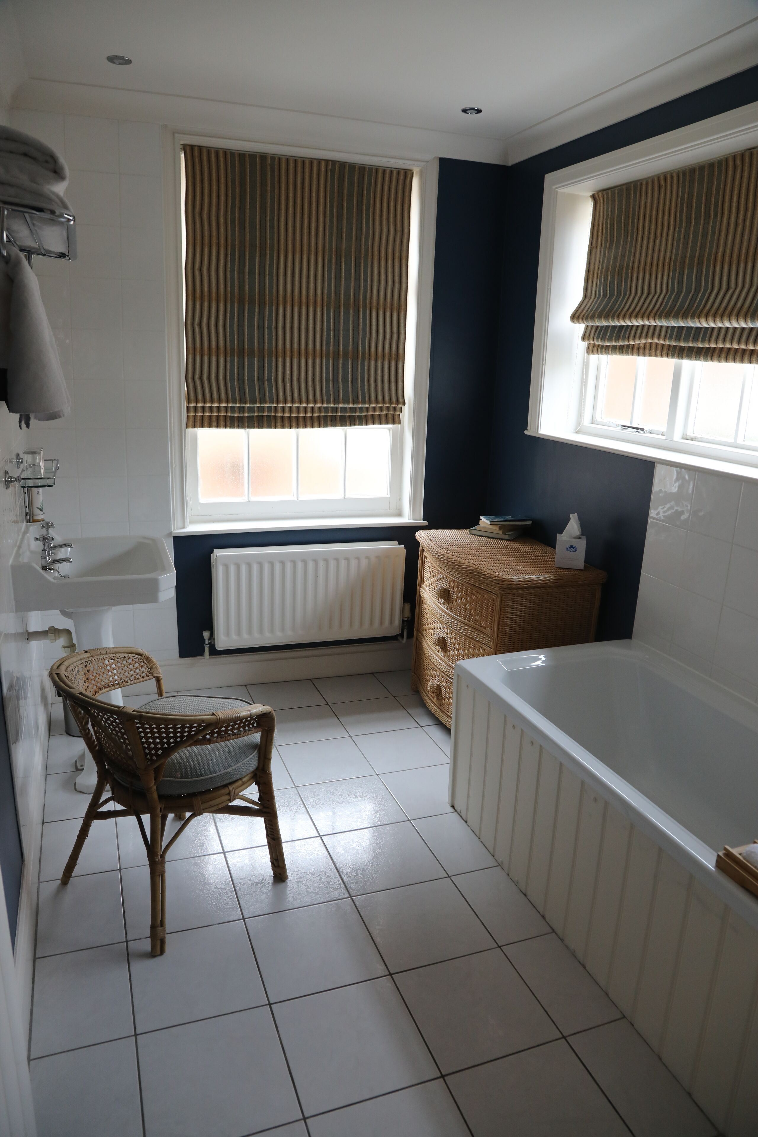 A bathroom with a bathtub, a sink, a wicker basket, and a chair.