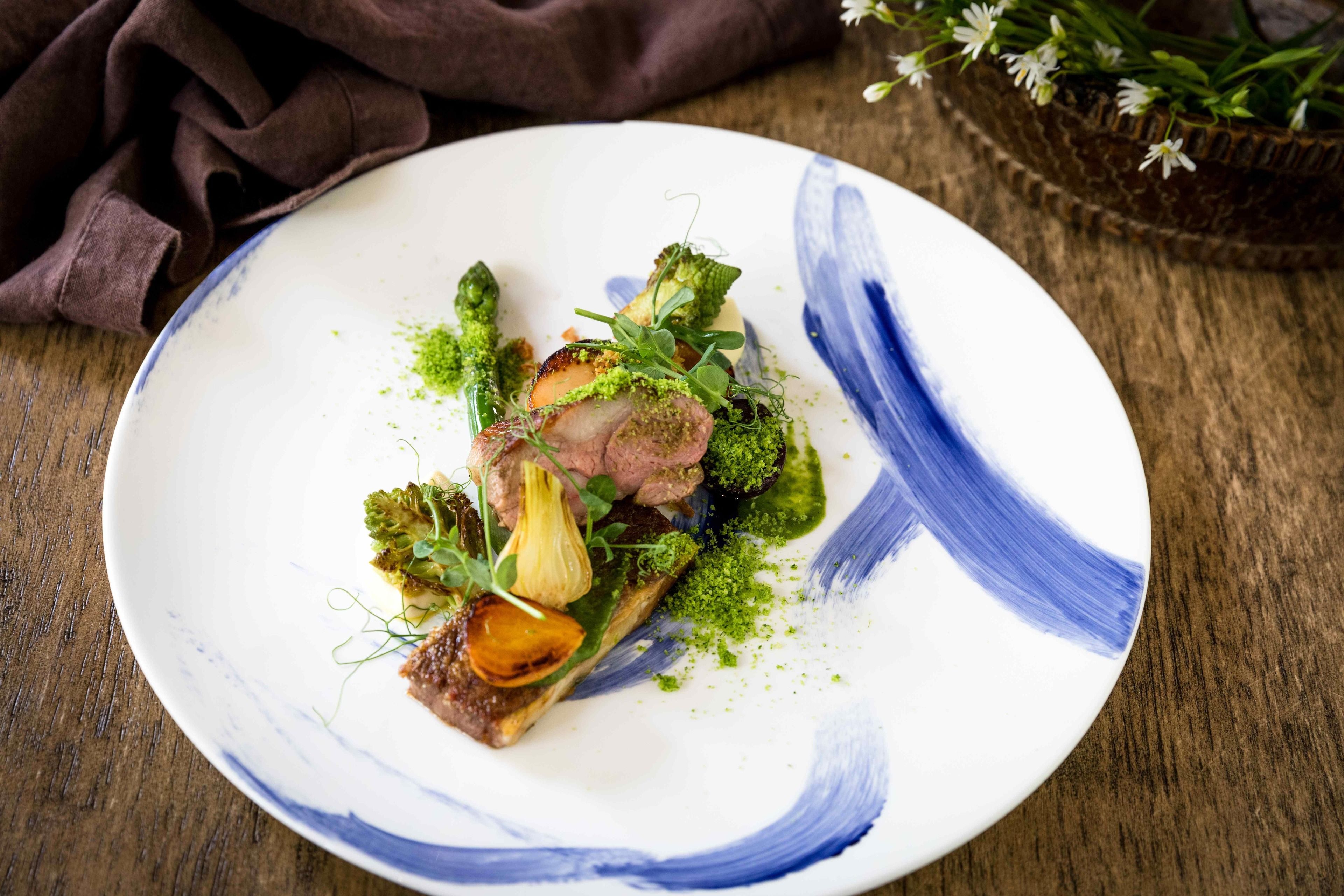 A plate of food with various vegetables and a piece of meat, served on a white plate with blue patterns.