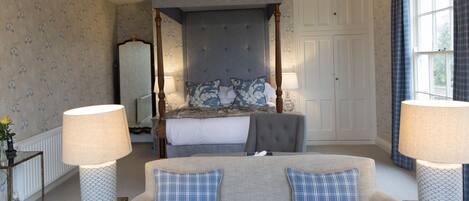 A bedroom with a four-poster bed, a sofa, two lamps, and patterned wallpaper.